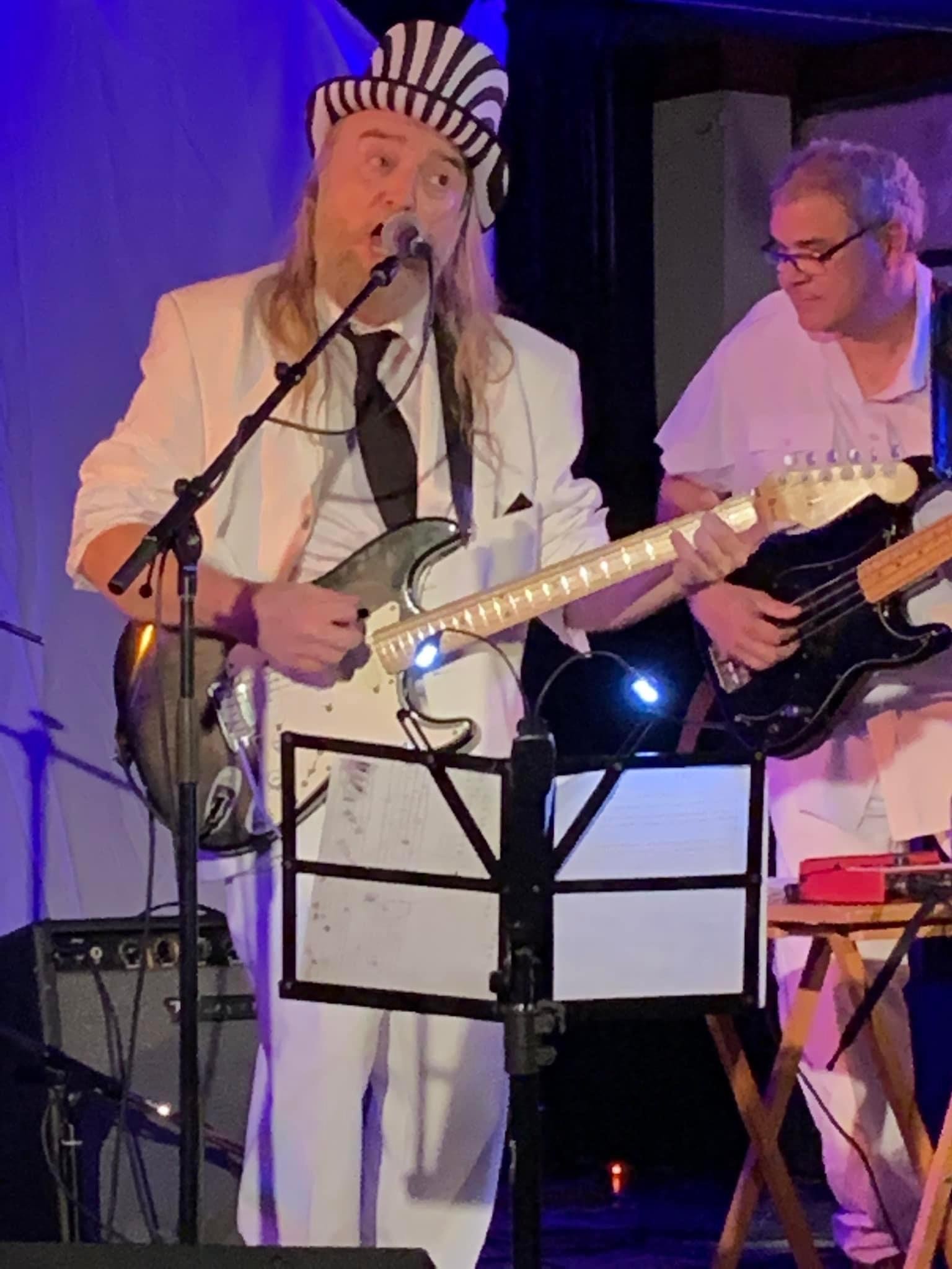 a man in a white suit and hat is playing a guitar