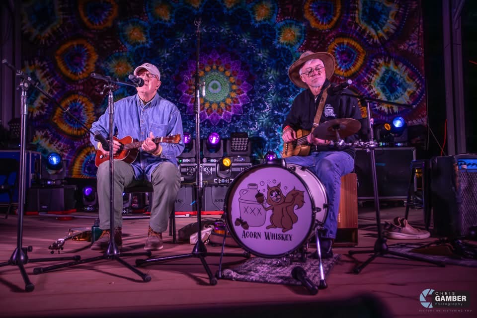 two men playing guitars on stage in front of a tapestry