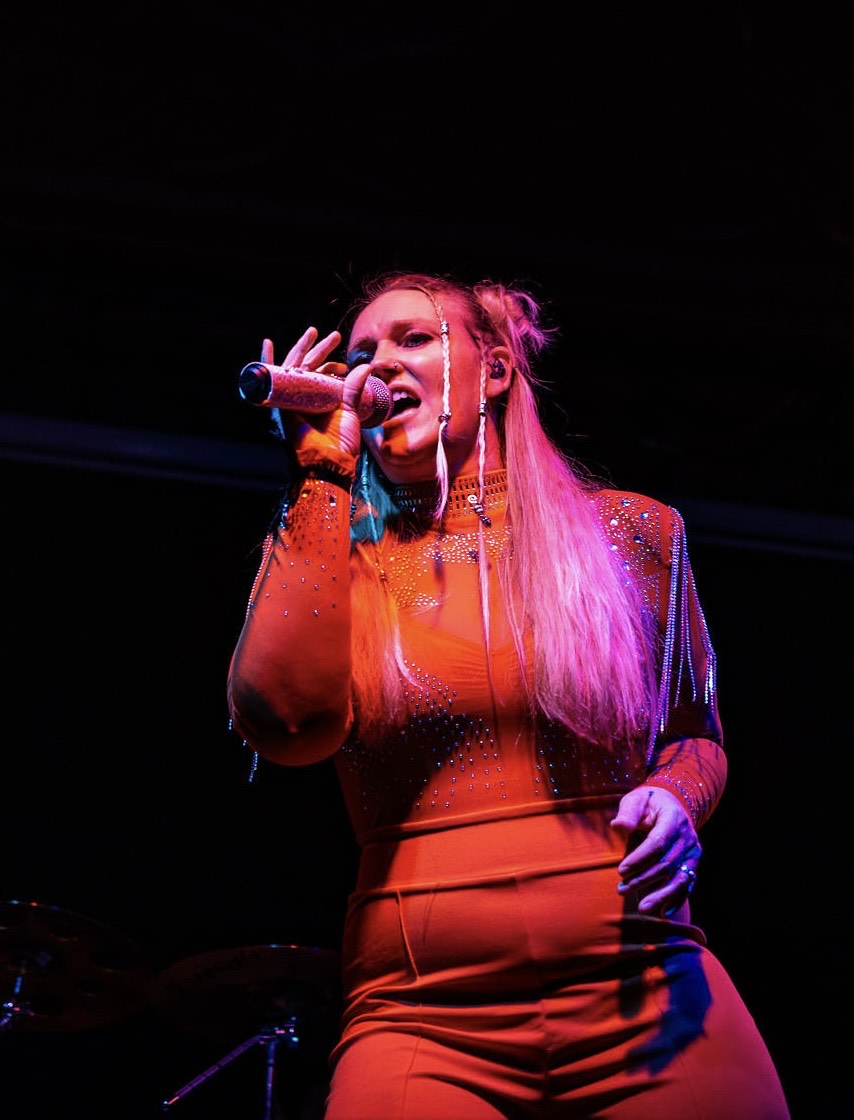 a woman in an orange jumpsuit singing into a microphone