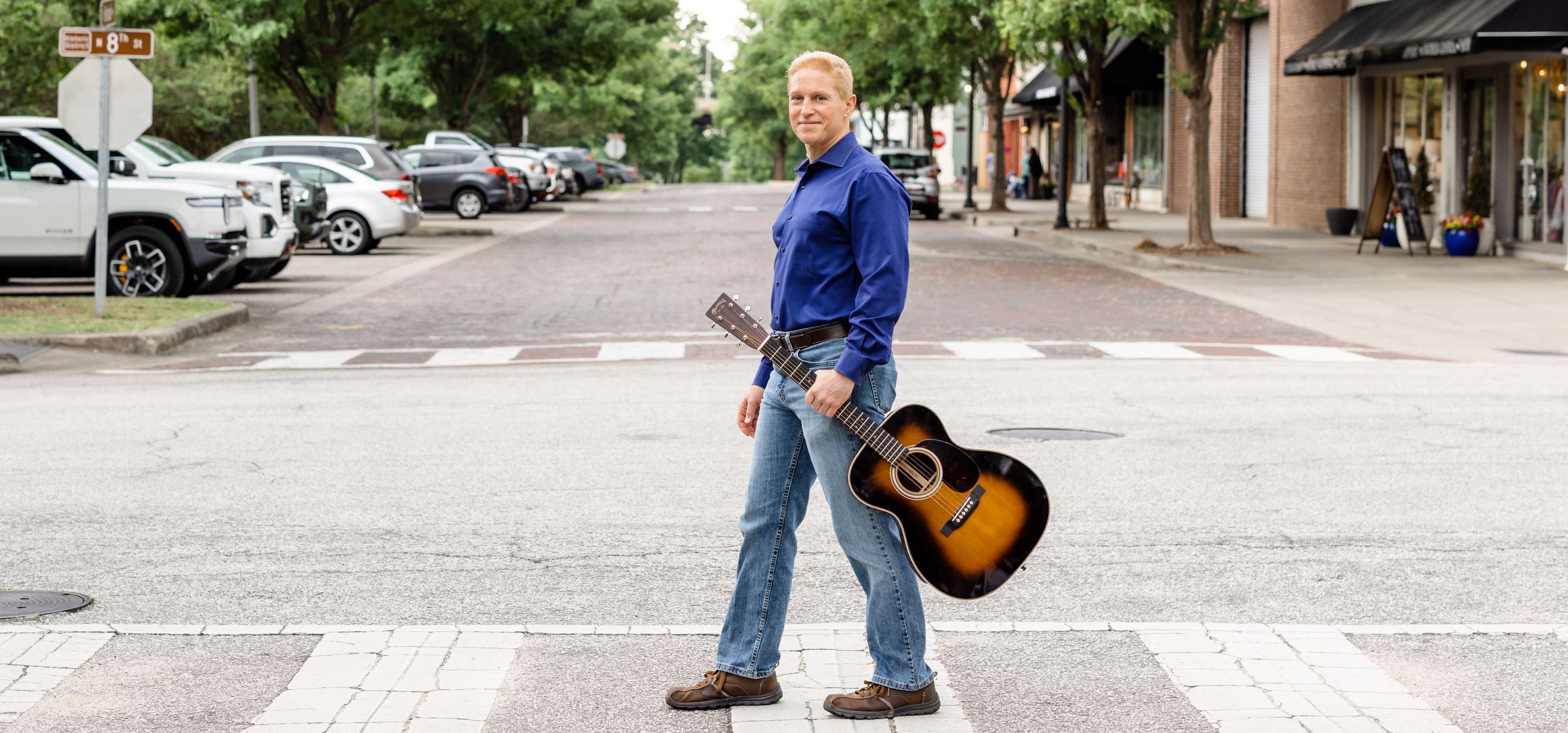 a man with a guitar standing in a crosswalk